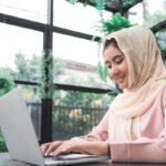 beautiful-young-smiling-asian-muslim-woman-working-laptop-sitting-living-room-home